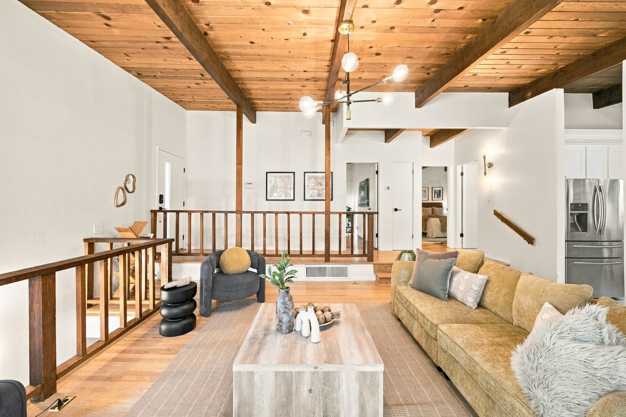 Living room with exposed wood ceiling beams, a tan sofa, and a raised dining area.