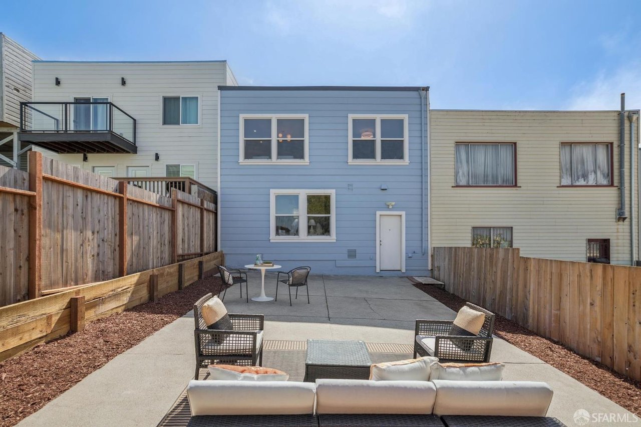 Fenced concrete patio behind a blue-sided home, staged with outdoor sofas, chairs, and a table.