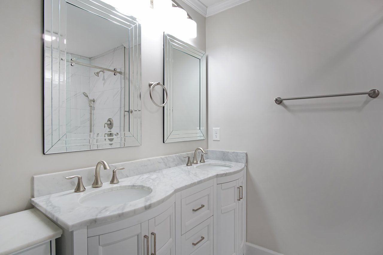 Elegant bathroom with white marble countertop, dual sinks, silver fixtures, mirrored medicine cabinets, and a sleek towel bar. Clean and modern design.