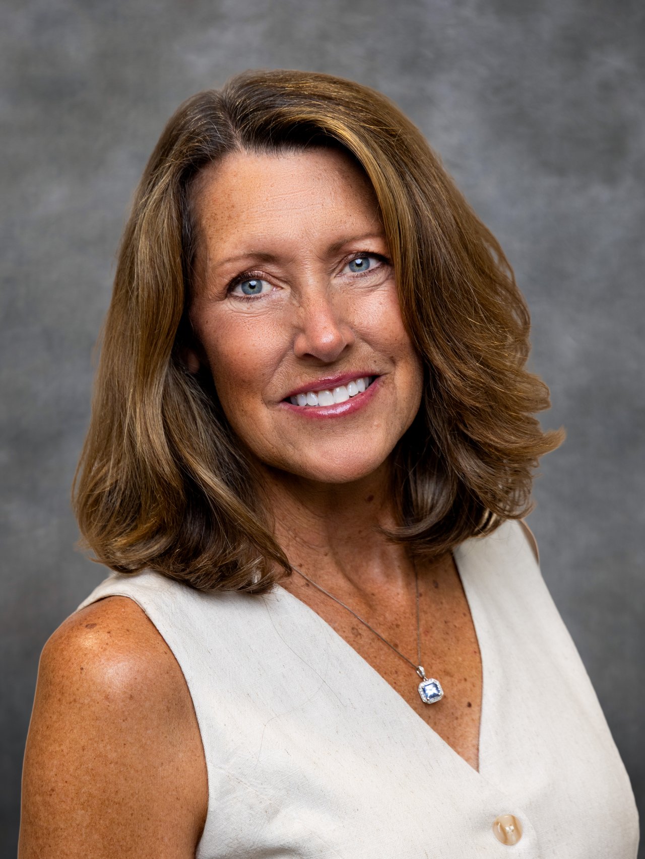 Laurie Wing smiling in a white sleeveless top and pendant necklace.