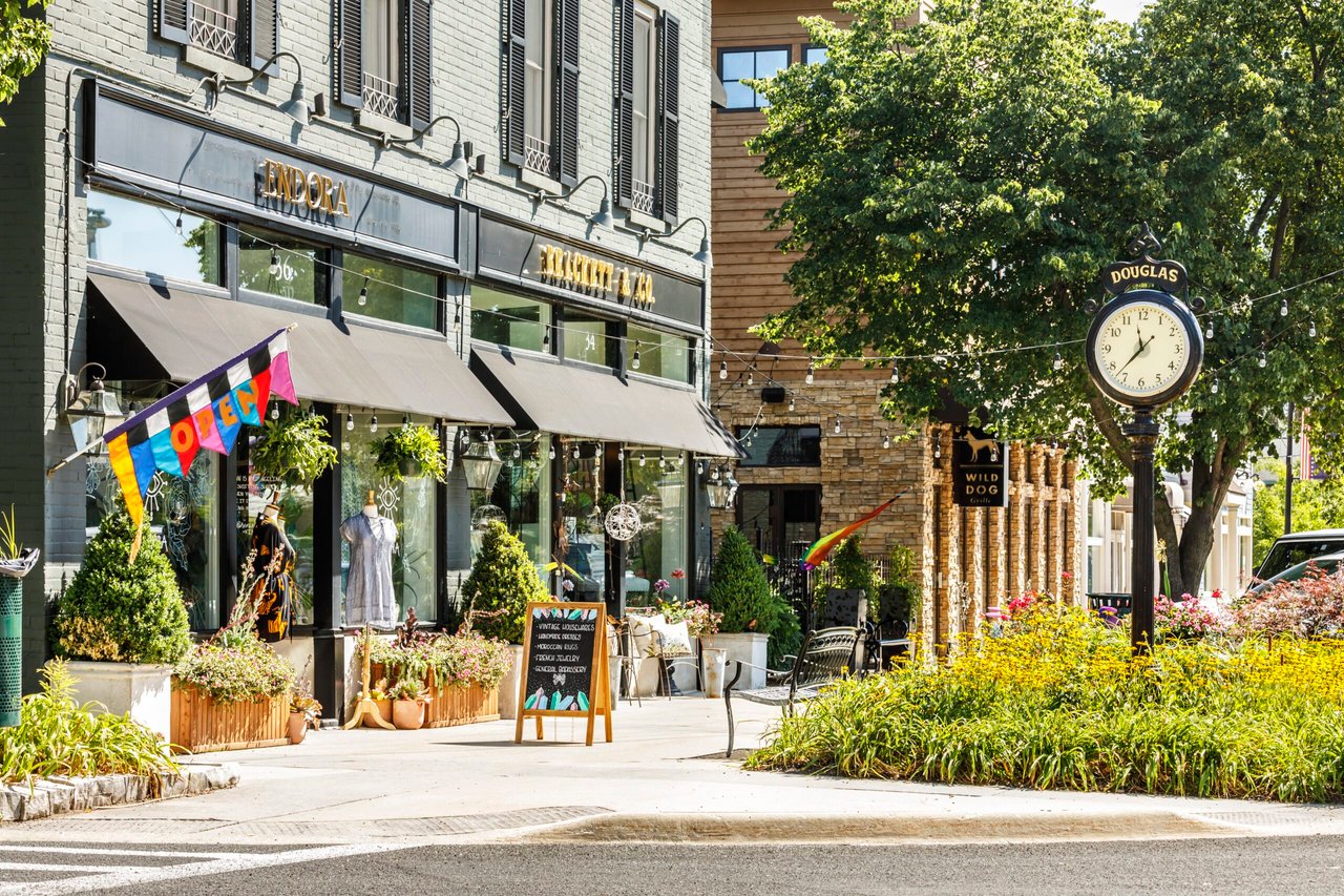 Shops and boutiques in downtown Douglas, Michigan, with a decorative clock and summer flowers along the street.