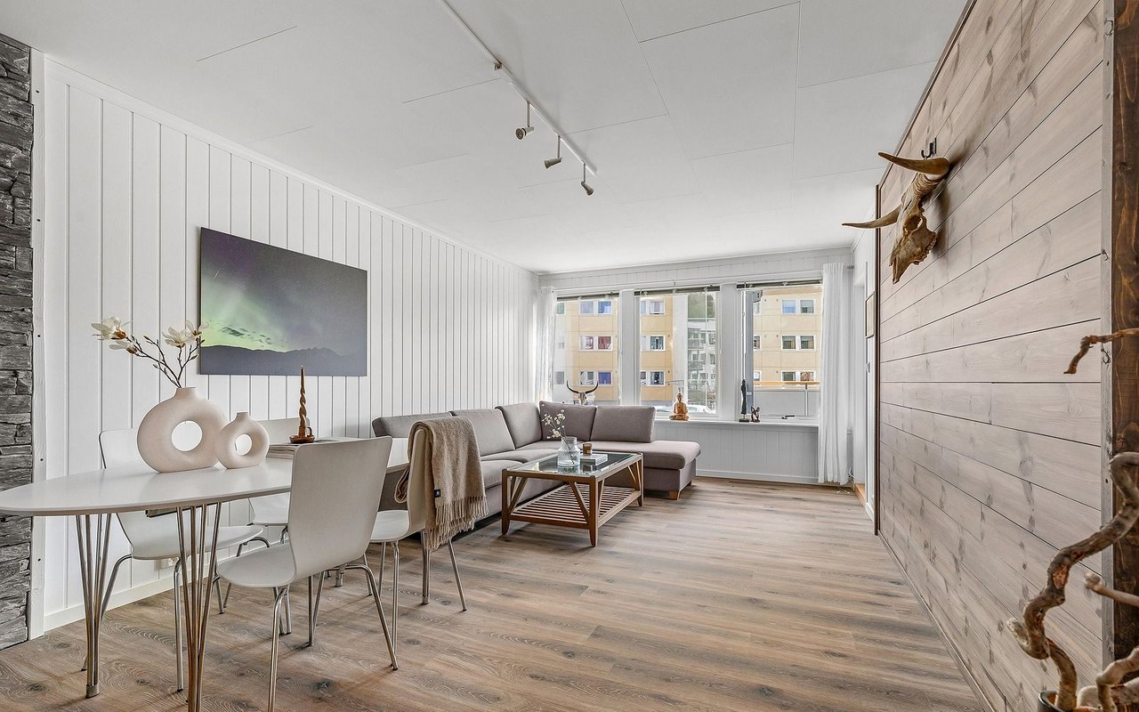 Open-plan living and dining room with a gray sectional, pale wood floors, and large windows.