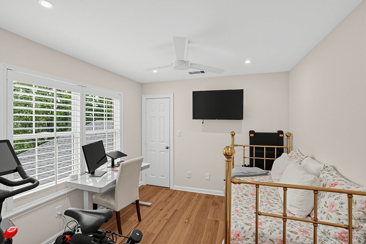 Bedroom with a brass bed, floral bedding, a desk by shuttered windows, and exercise equipment.