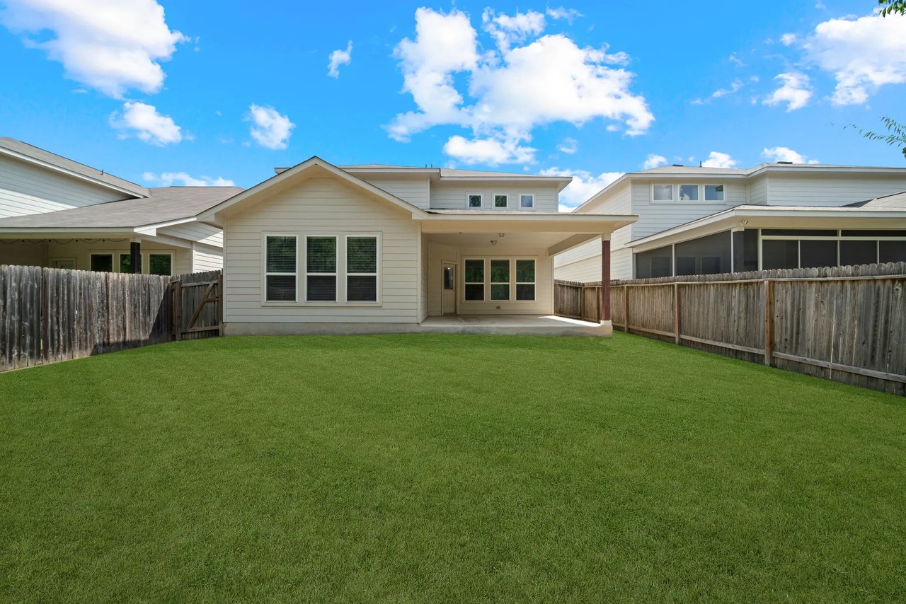 House rear with covered patio, fenced lawn, and neighboring homes.