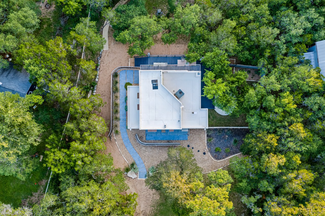 Aerial view of a modern home surrounded by dense trees, with curved paths and landscaped gravel areas.