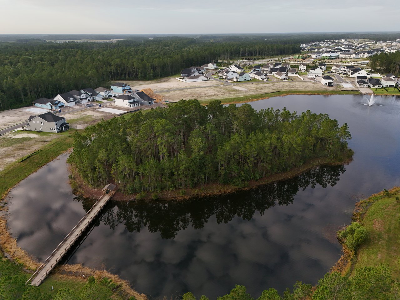 Aerial view of a wooded island, pedestrian bridge, surrounding lake, and new homes at Silverleaf.