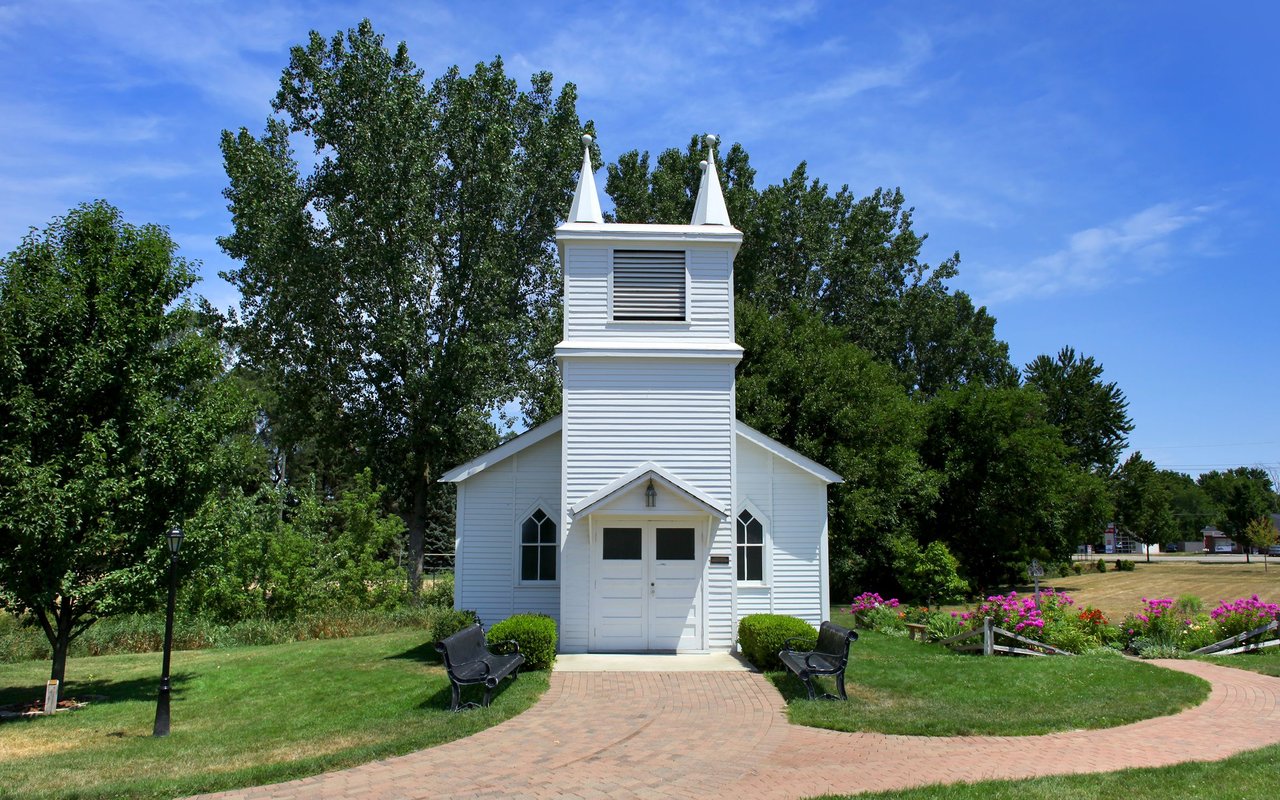 White church with twin steeples beside a curved brick walkway and flower beds.