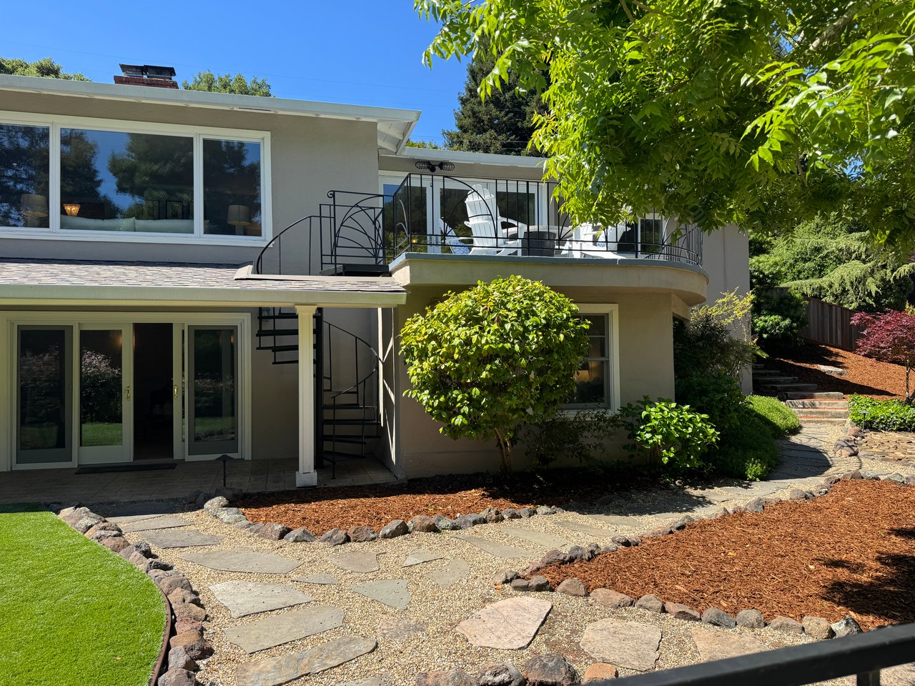 Modern two-story home with a balcony, spiral staircase, and landscaped stone paths.