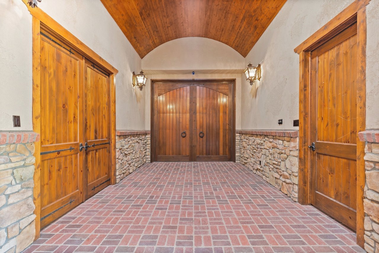 Barn entrance with arched wooden doors, brick flooring, stone walls, and a vaulted wood ceiling.