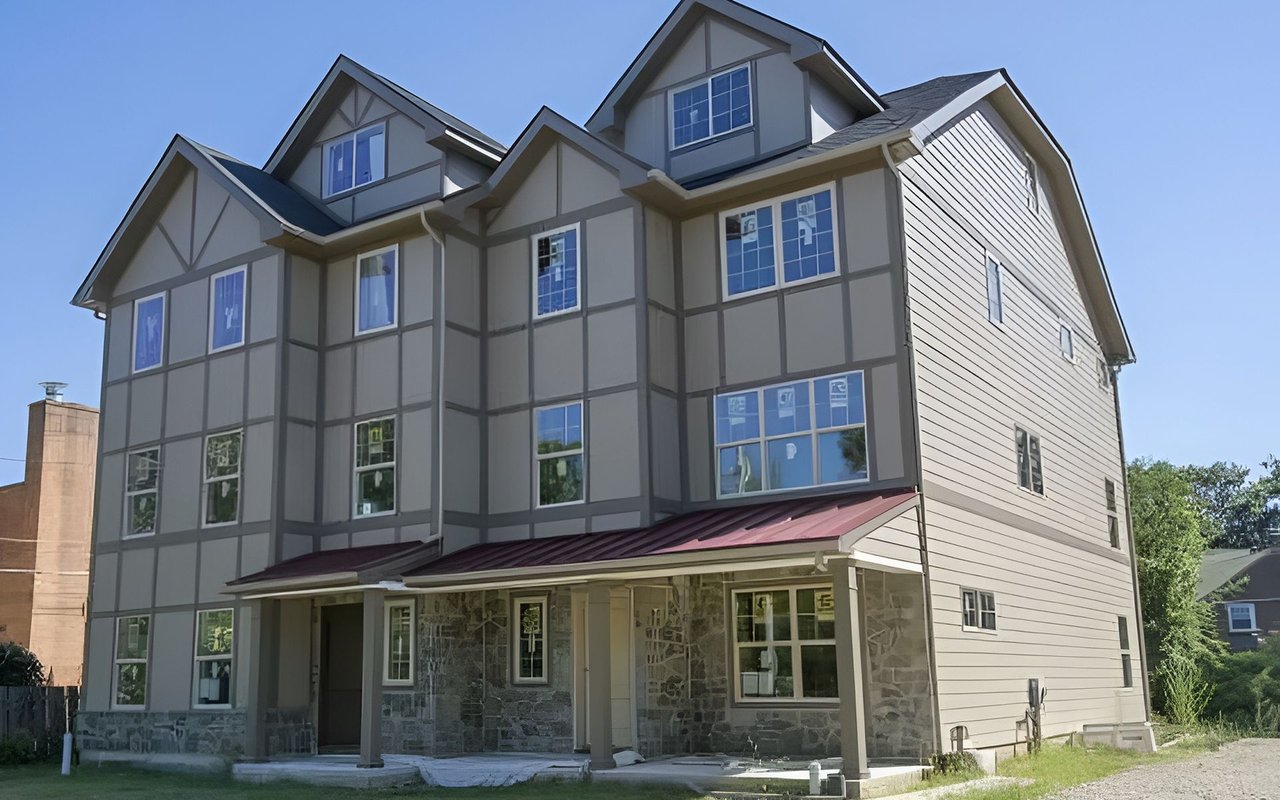 Multi-story townhome-style building with gabled roofs, stone lower walls, and red metal porch roofs.