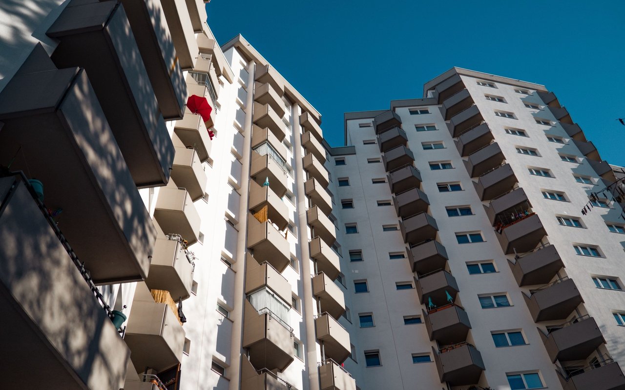 Condominium buildings with rows of balconies viewed from below against a clear blue sky.
