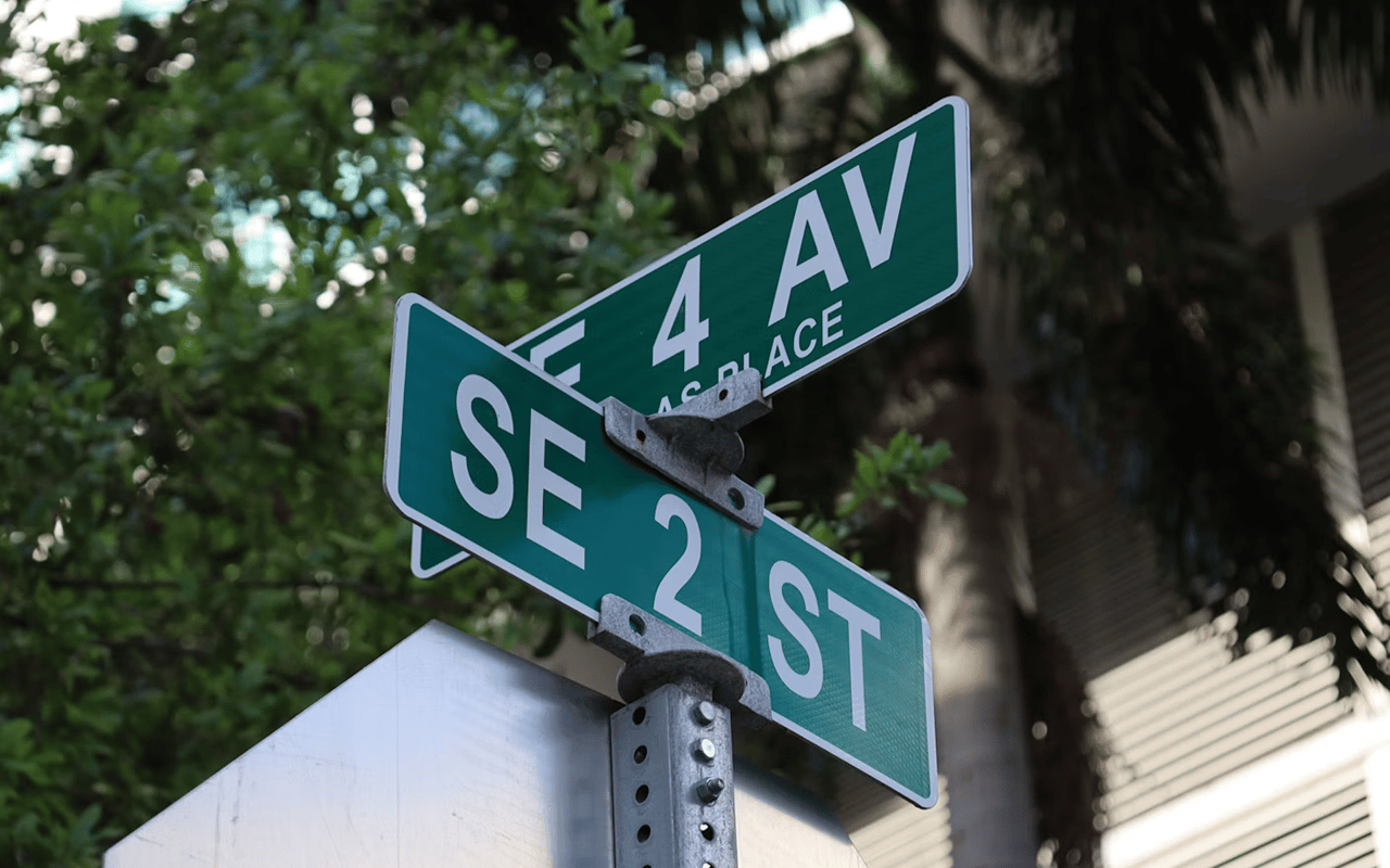 Street signs for 4 Avenue and Southeast 2nd Street among tropical foliage.