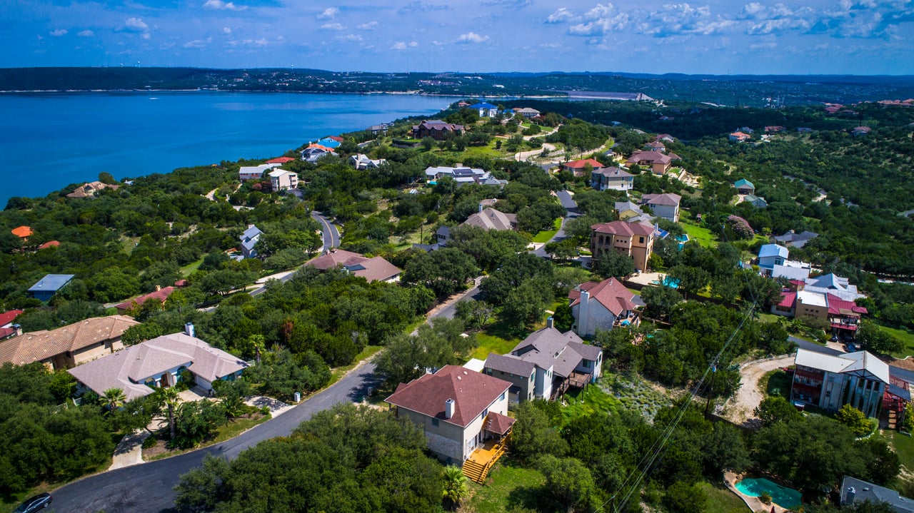 Aerial view of a wooded lakeside neighborhood with winding roads and scattered homes.
