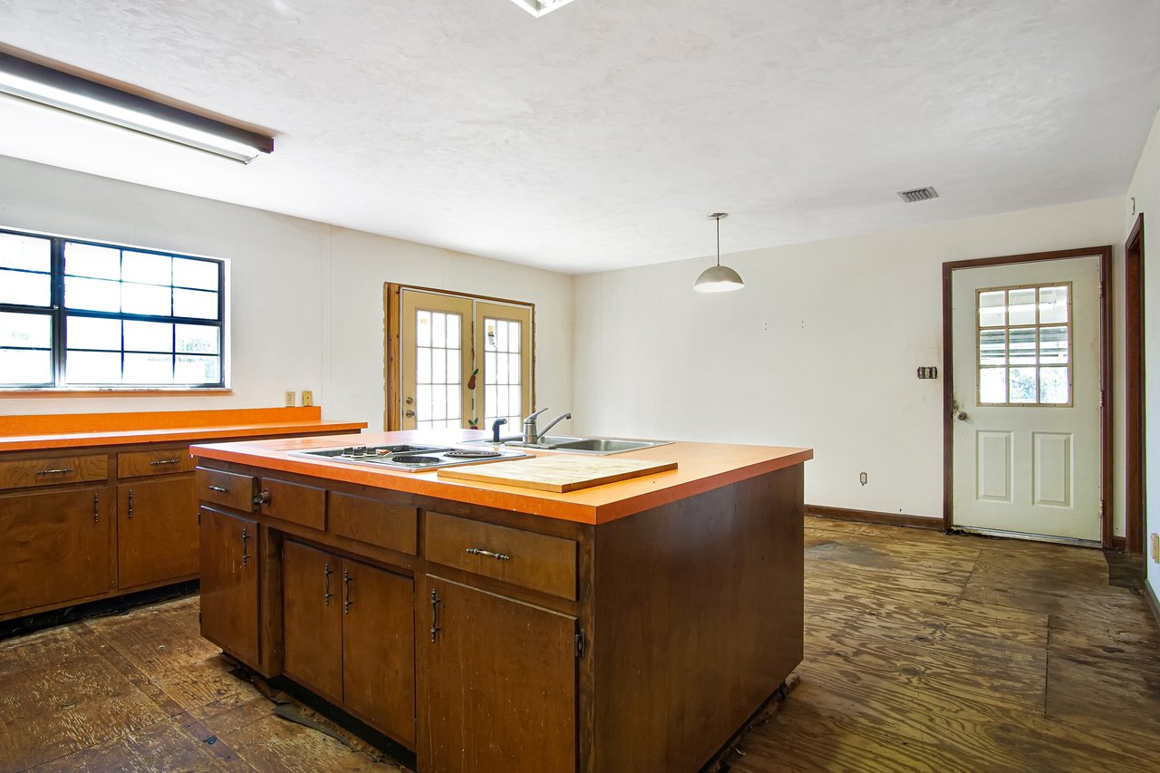 Spacious kitchen with wooden cabinets and orange countertops. Central island features a sink and cooktop. Large windows and doors provide ample light.