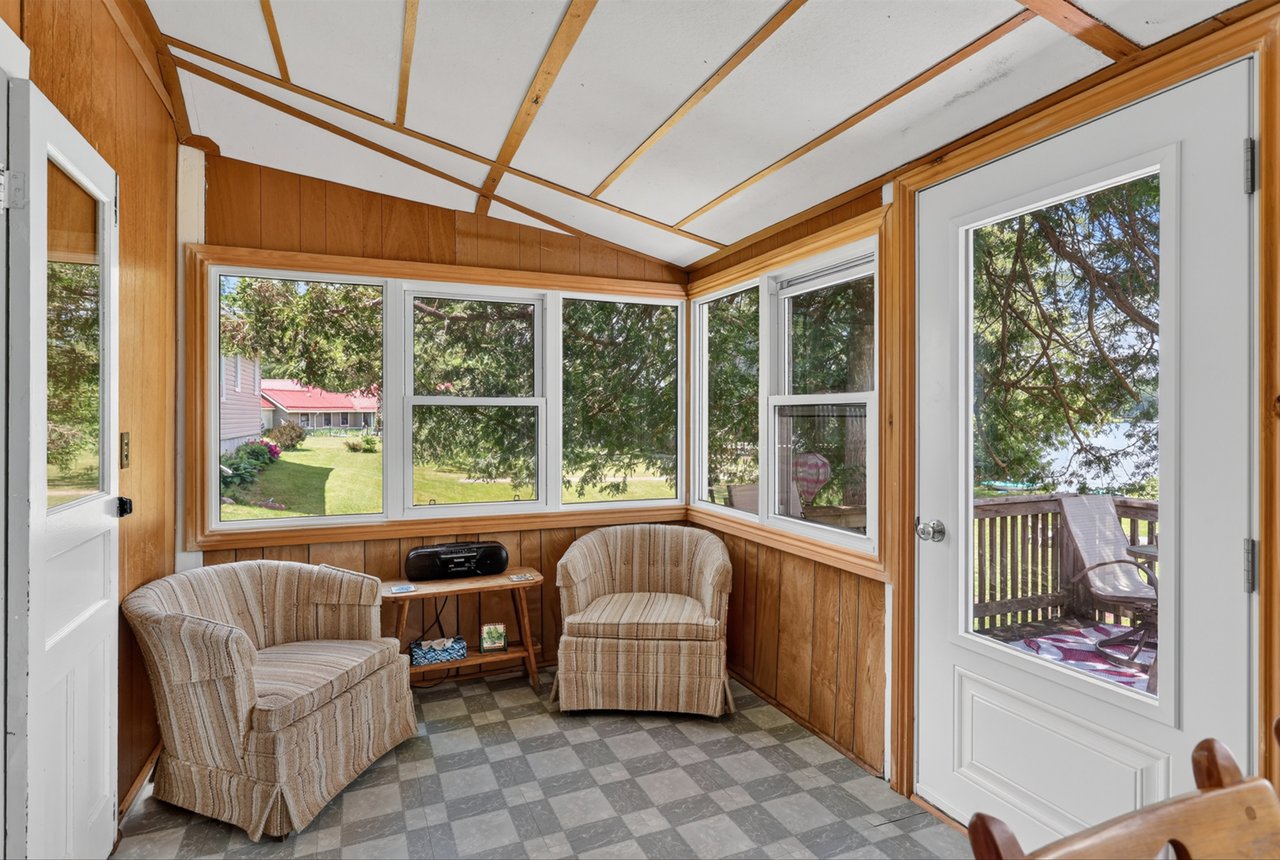 Sunroom with two upholstered armchairs, wood-paneled walls, and windows overlooking a lawn and deck.