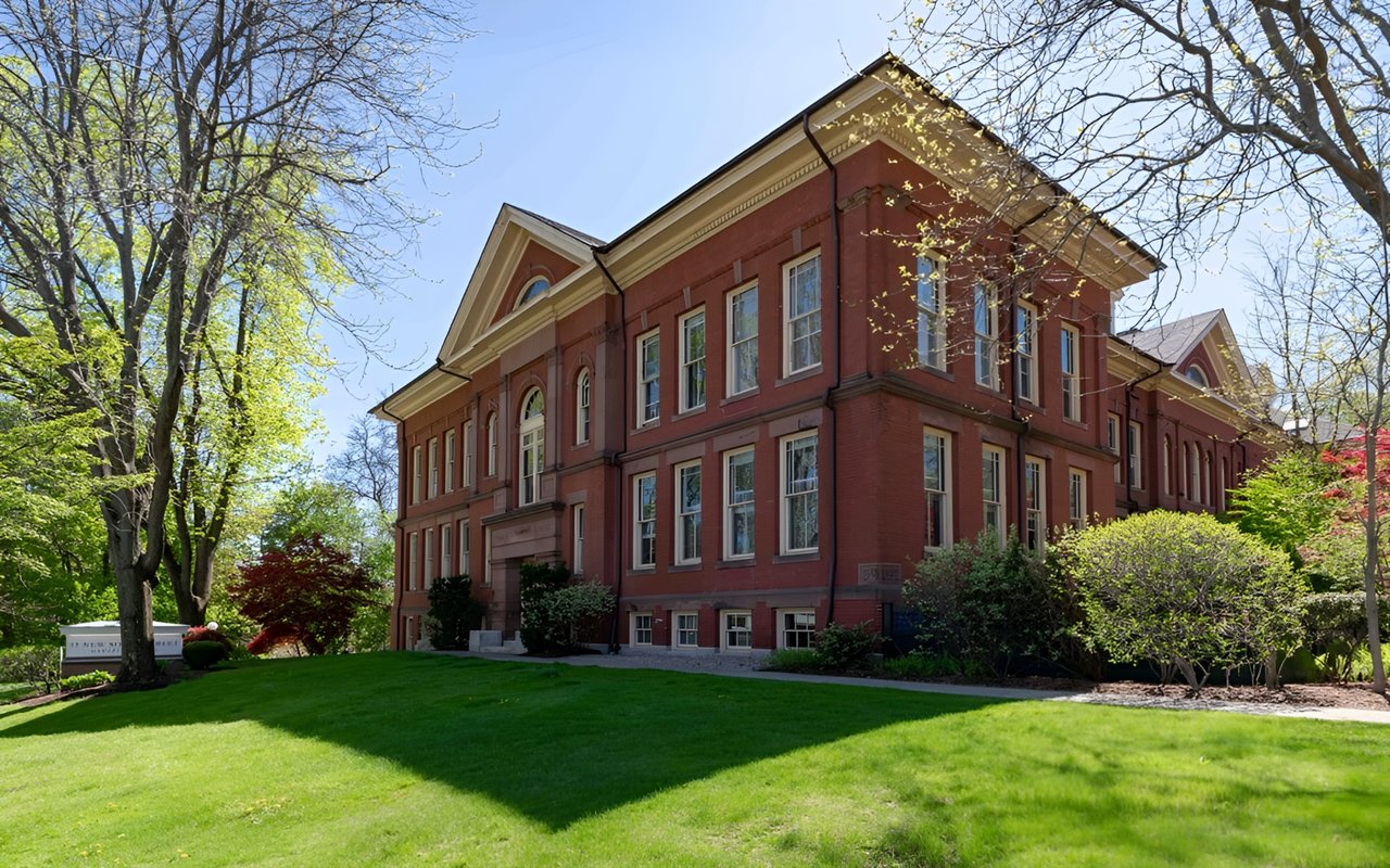 Red-brick condominium building with light trim, a broad green lawn, and mature trees.
