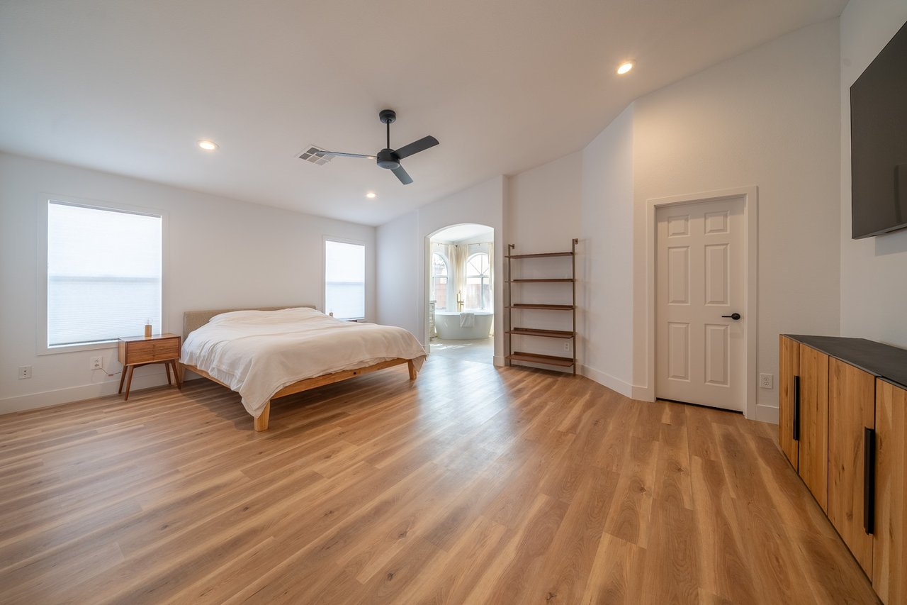 Bedroom with a low wooden bed, warm wood floors, and an arched opening to a bathroom tub.