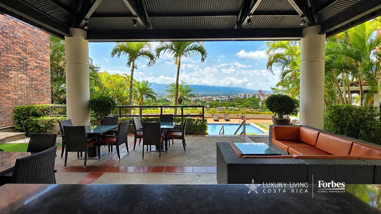 Condominium terrace with outdoor dining and lounge seating overlooking a pool, cityscape, and distant mountains.