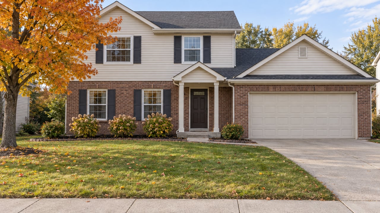Brick-and-ivory-siding two-story home behind a broad autumn lawn, with a sugar maple and neatly edged hydrangea beds.