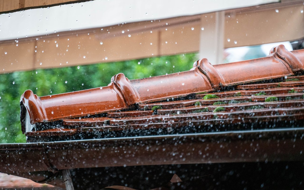 Rain falls across reddish roof tiles and a dark gutter.