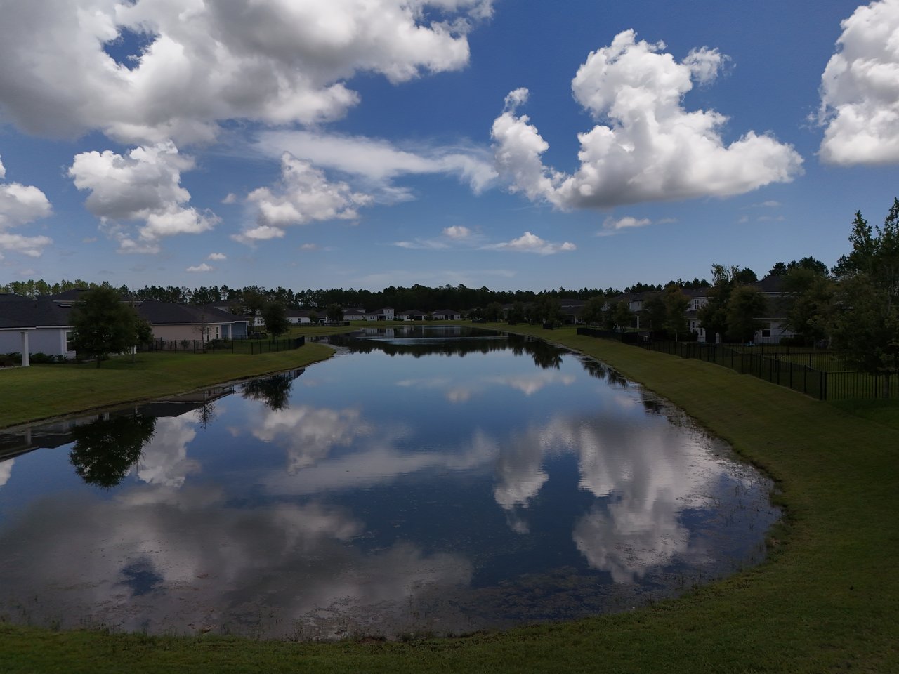 Neighborhood pond reflecting clouds, bordered by grassy banks and homes.