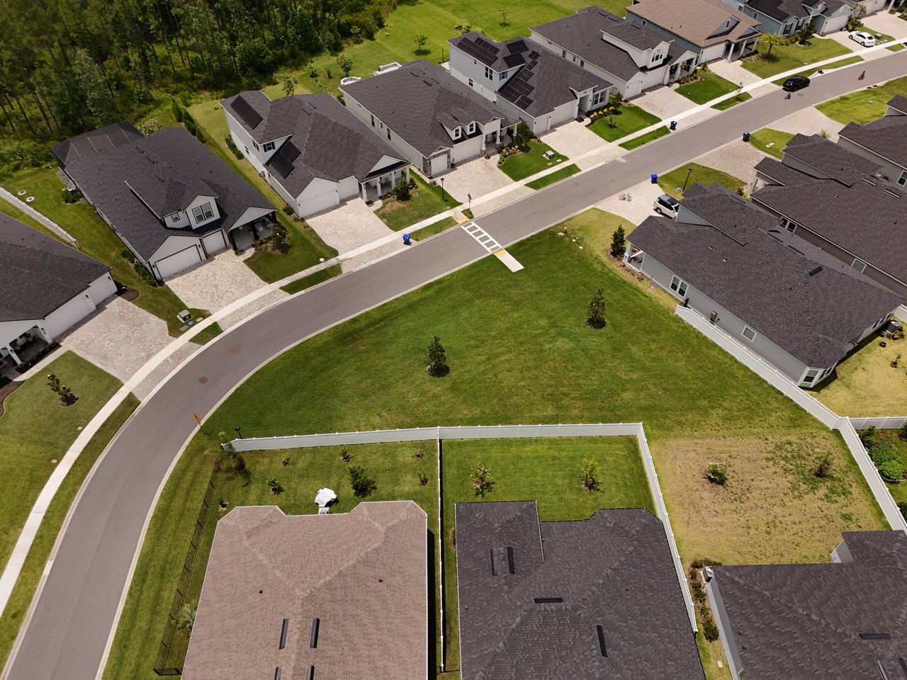 Aerial view of homes along a curved neighborhood street beside a wooded edge.