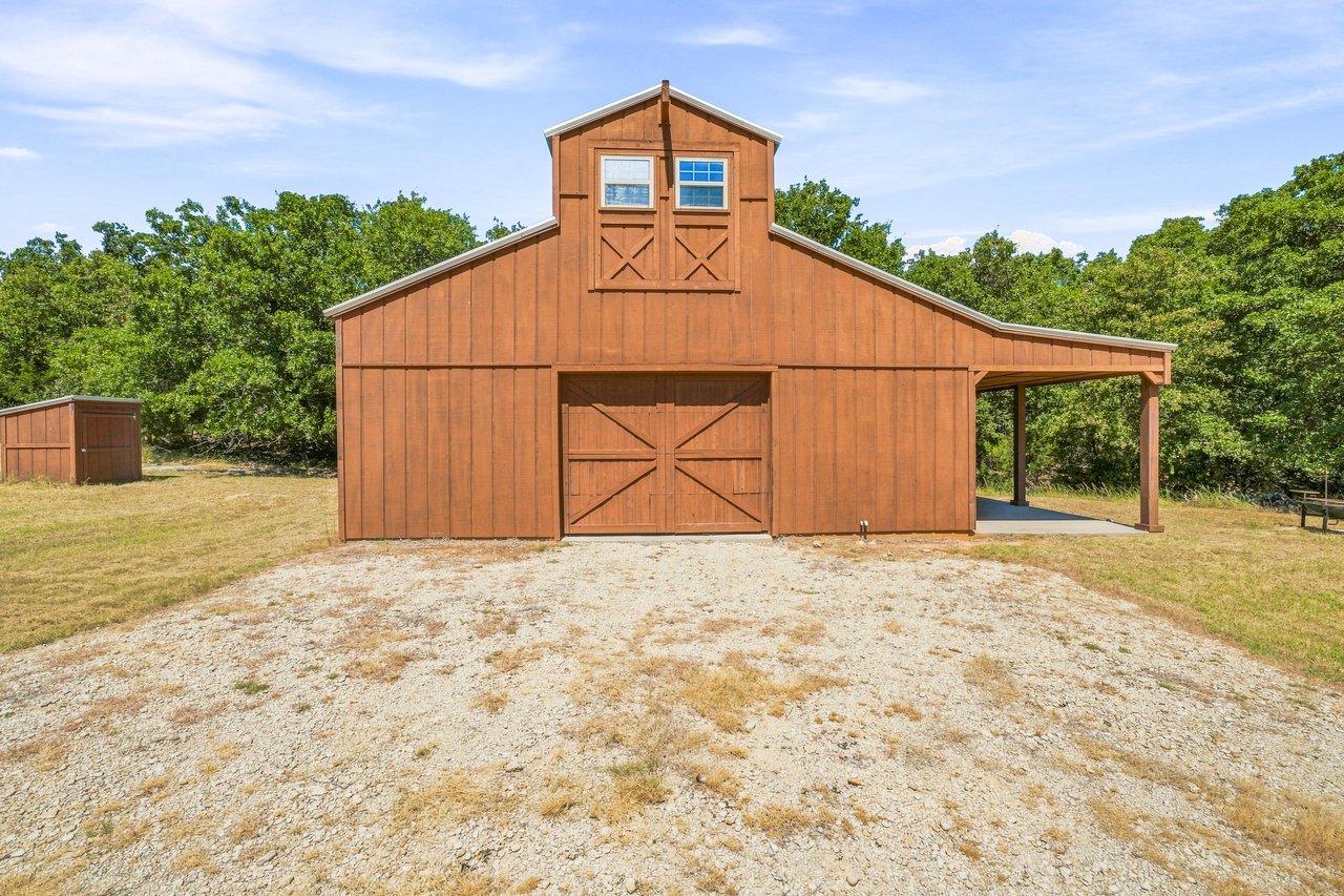 Brown wooden barn with upper windows, large double doors, and an open-sided covered bay.