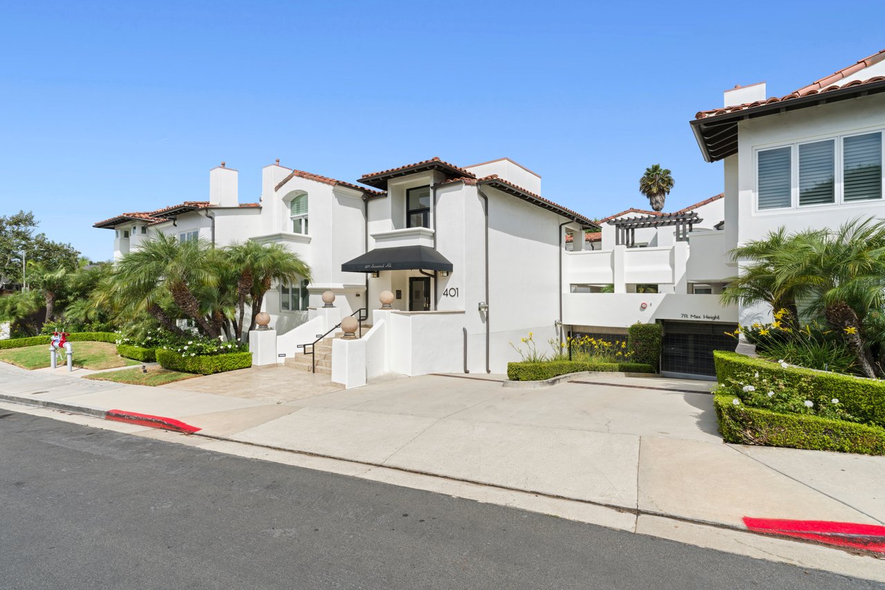 White stucco Spanish-style building with red tile roofs, palm landscaping, and a black entrance awning.
