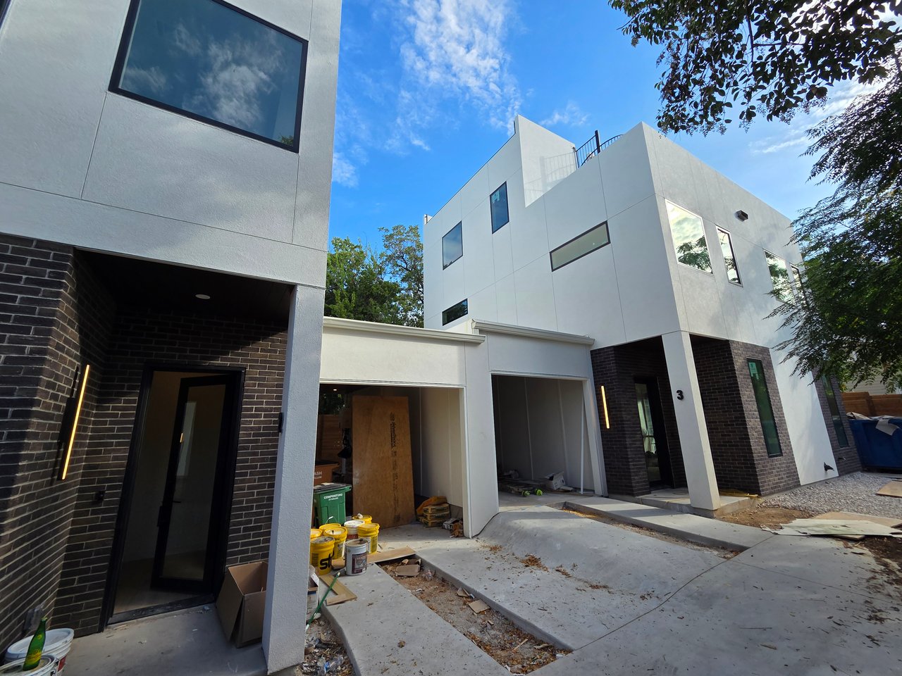 Modern white and dark-brick homes under construction, with unfinished driveways and materials in front.
