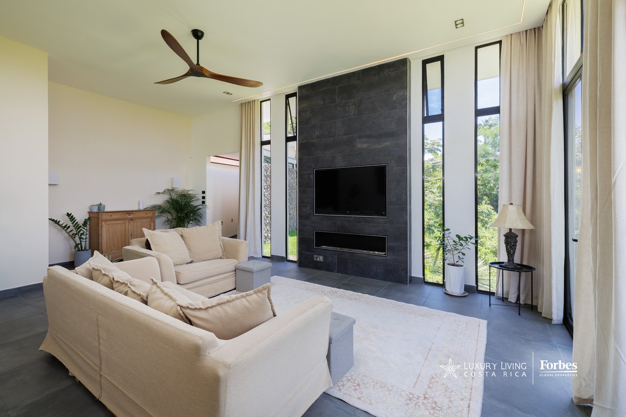 Contemporary living room with cream sofas, a dark stone fireplace wall, and tall windows overlooking greenery.