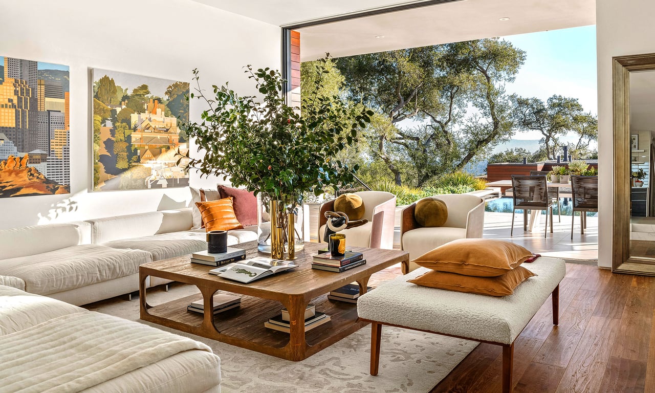 Living room with white sofas and a wood coffee table, opening onto a patio and pool.