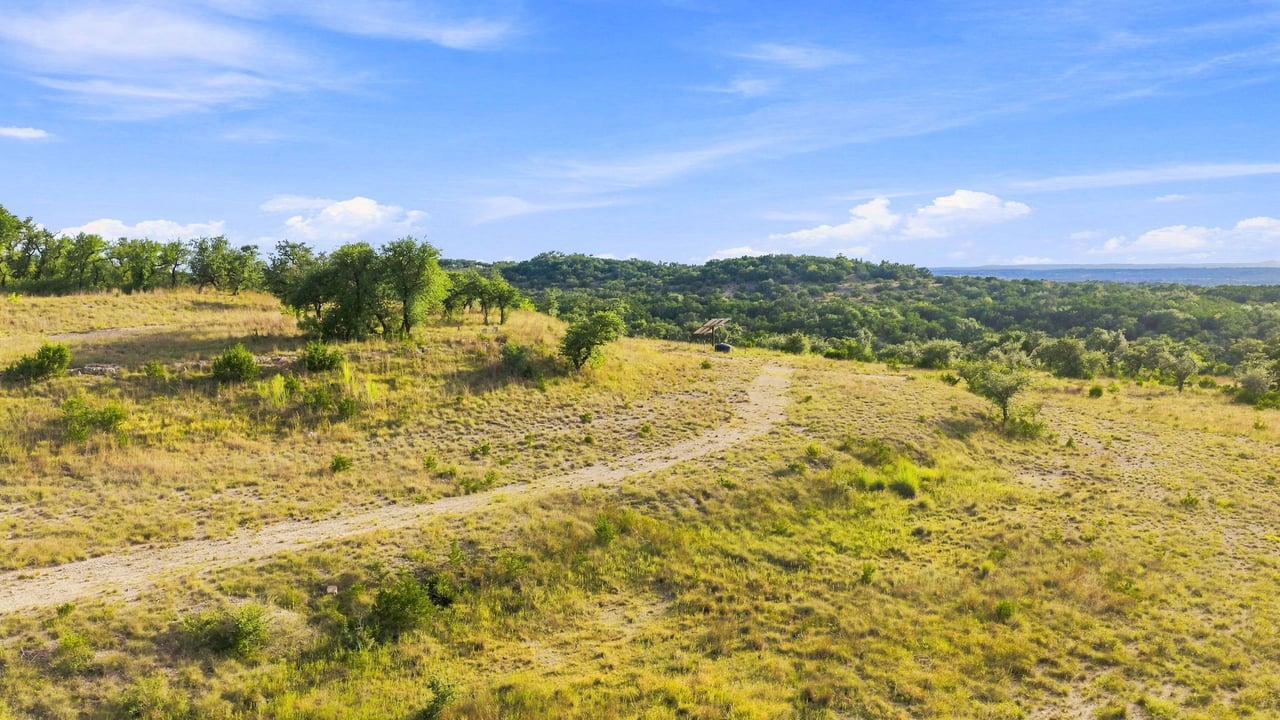 Aerial view of open Texas Hill Country ranchland with scattered trees and rolling wooded hills.