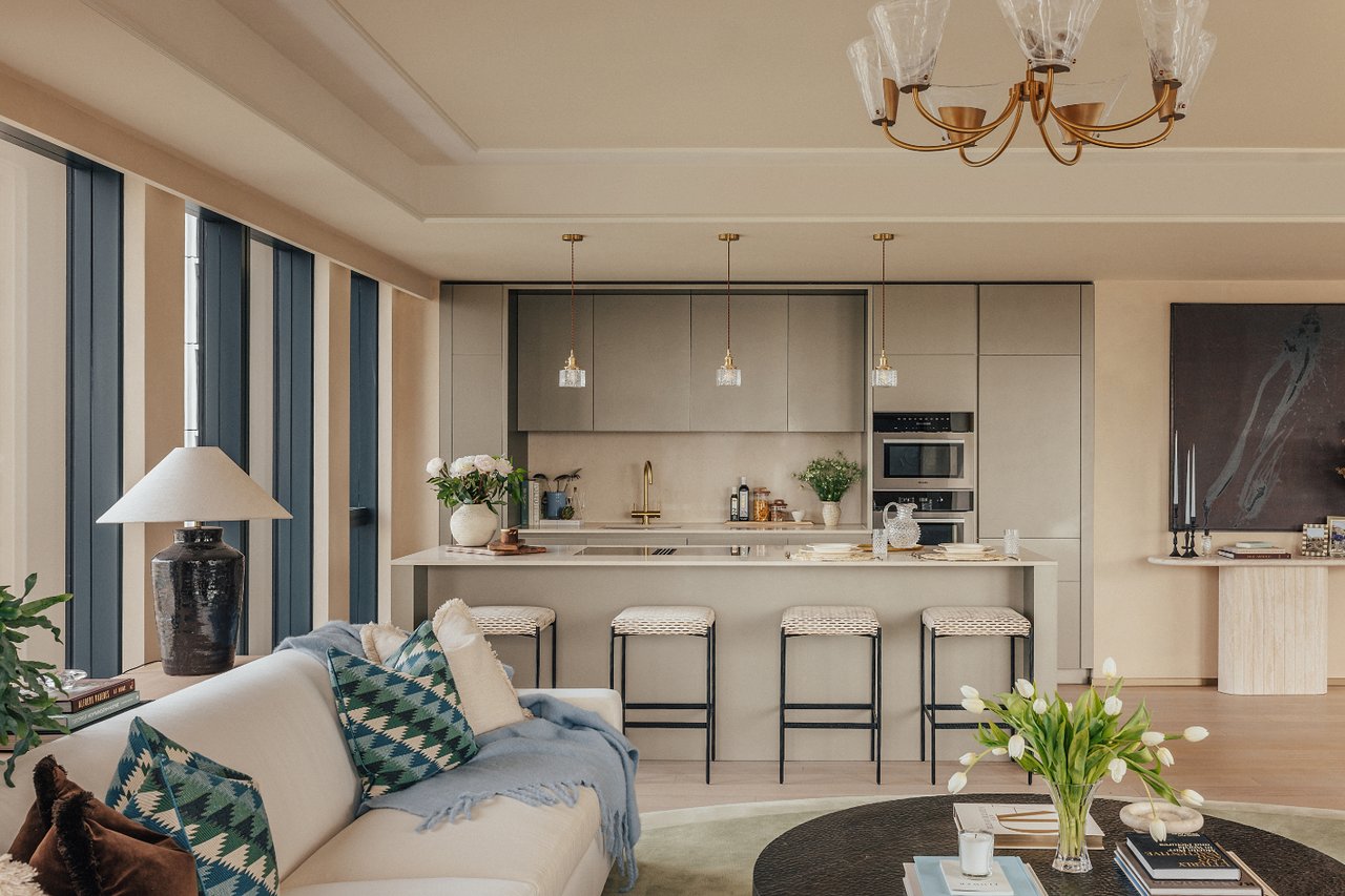 Open-plan living room and kitchen with a marble island, four bar stools and tall windows.