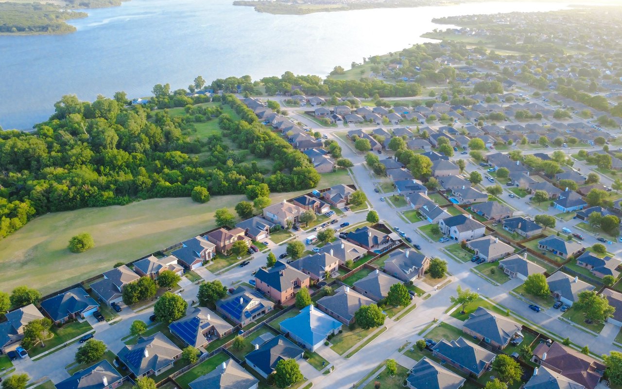 Aerial view of homes beside a lake, with a wooded greenbelt along the shoreline.