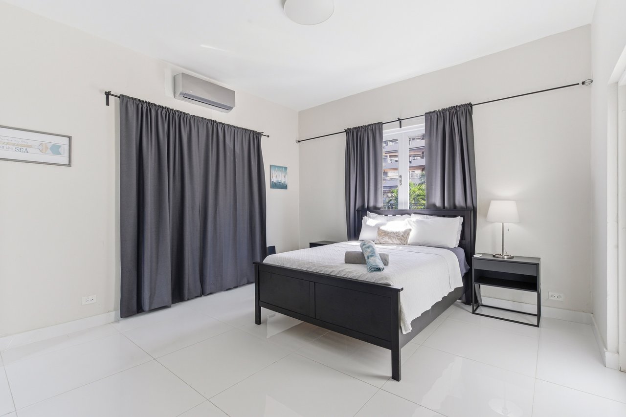 Bedroom with a black bed frame, white bedding, gray curtains, and a teal towel folded on the bed.