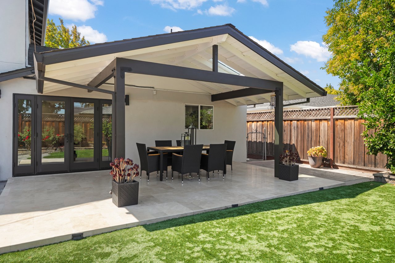 Covered backyard patio with outdoor dining set, folding glass doors, and a green lawn.
