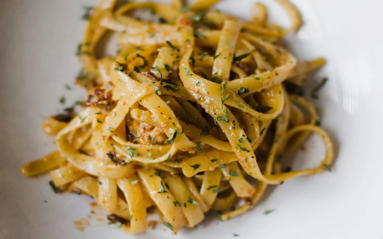  A close-up of a bowl of pasta, likely fettuccine, with a light sauce and garnished with fresh herbs.