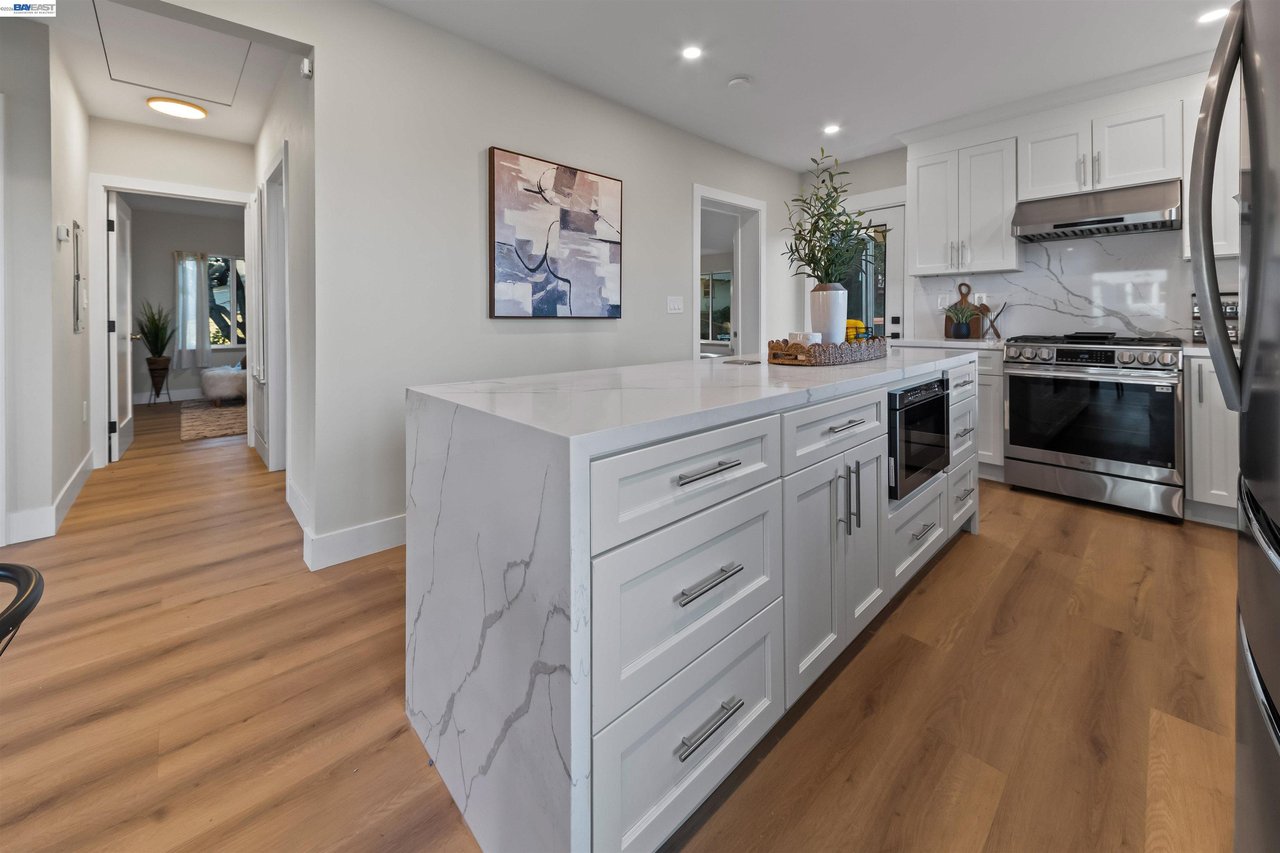 Kitchen with a large marble-look island, white cabinets, stainless steel appliances, and wood floors.