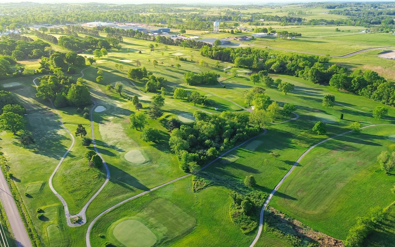 Aerial view of a golf course with rolling fairways, putting greens, and winding cart paths.