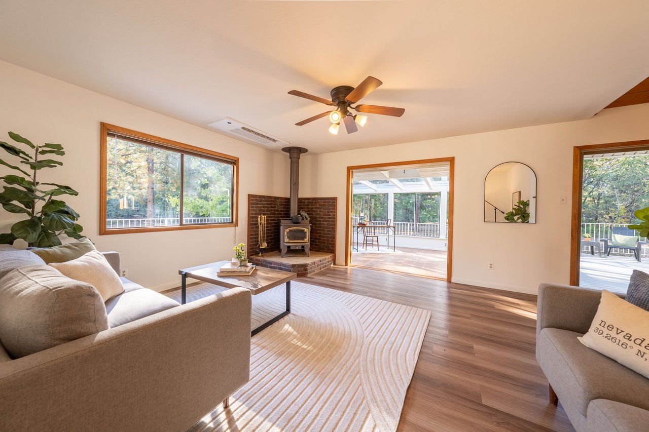Living room with a brick-backed wood stove, large windows, and access to a covered deck.