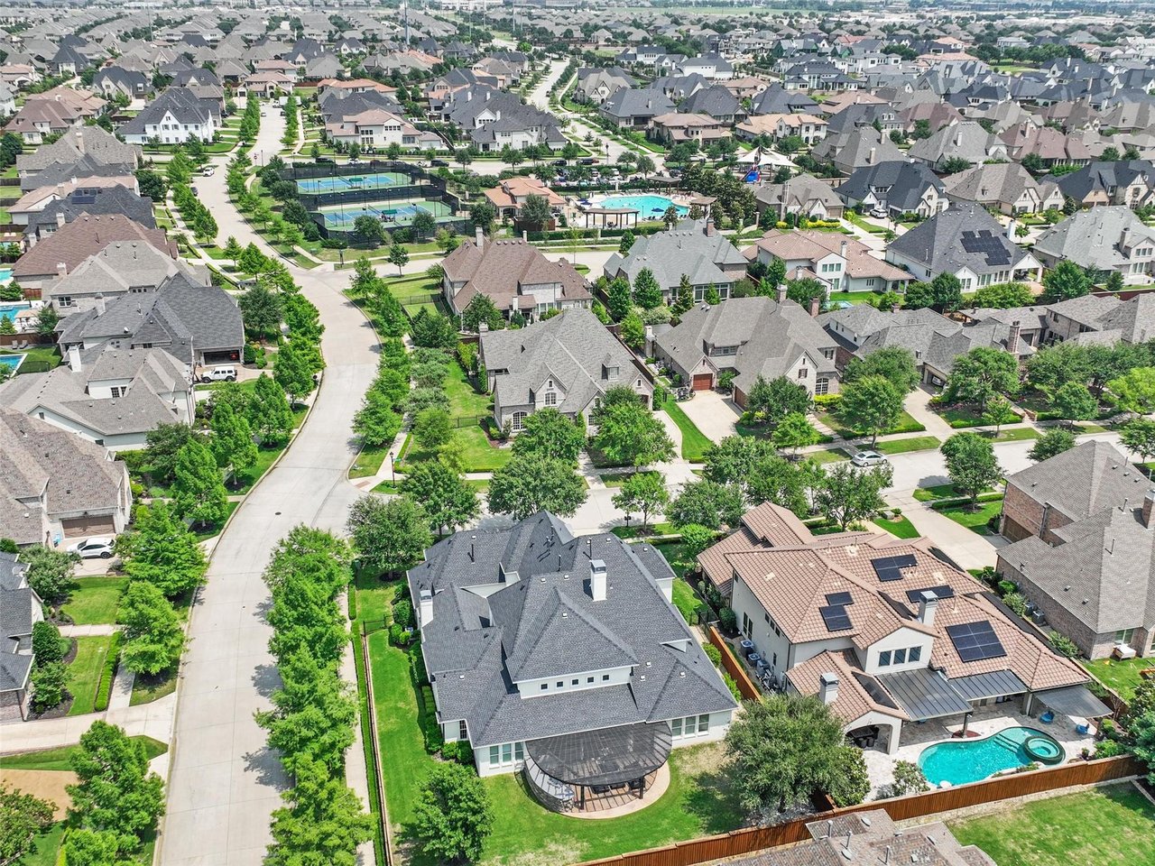Aerial drone view of Newman Village in Frisco TX showing luxury homes, tree-lined streets, pool and tennis court amenities in this premier North DFW community.