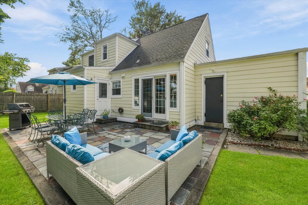Stone patio with wicker seating and blue cushions behind a light-colored house.