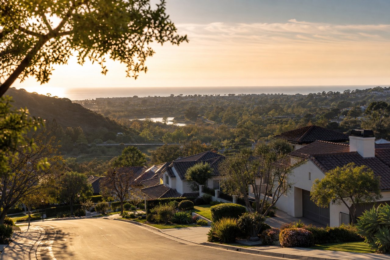 Hillside homes overlook a coastal neighborhood and ocean in warm evening light.
