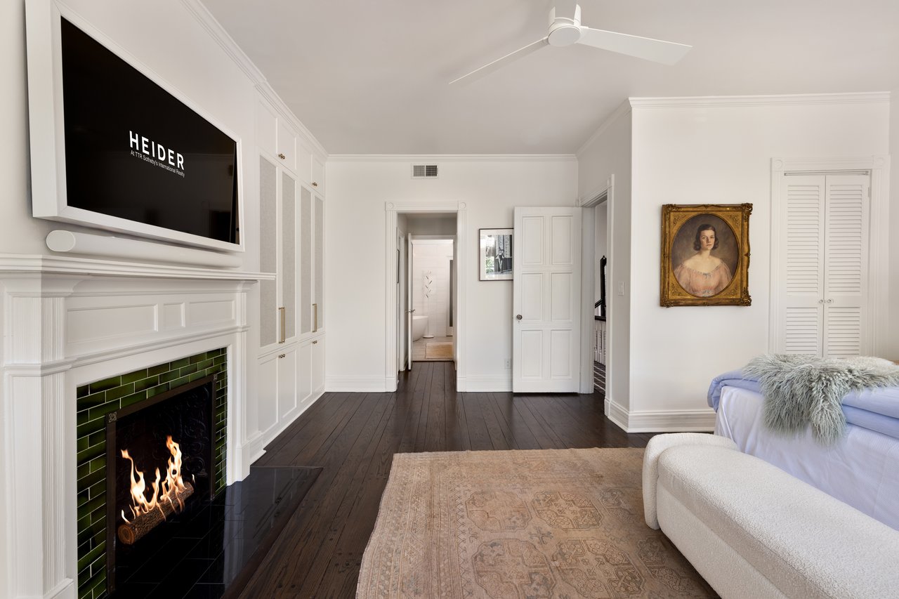 Furnished bedroom with a green-tile fireplace, built-in cabinets, and a bed beneath a portrait.