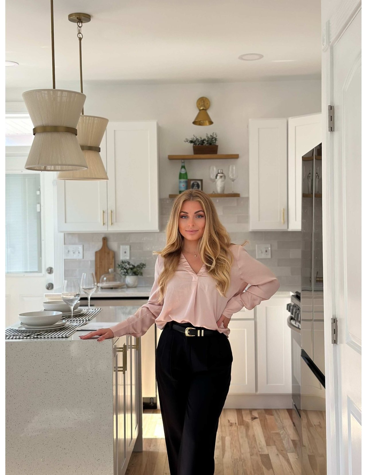 Mykala Smith standing beside a kitchen island in a bright kitchen, wearing a blush blouse and black trousers.