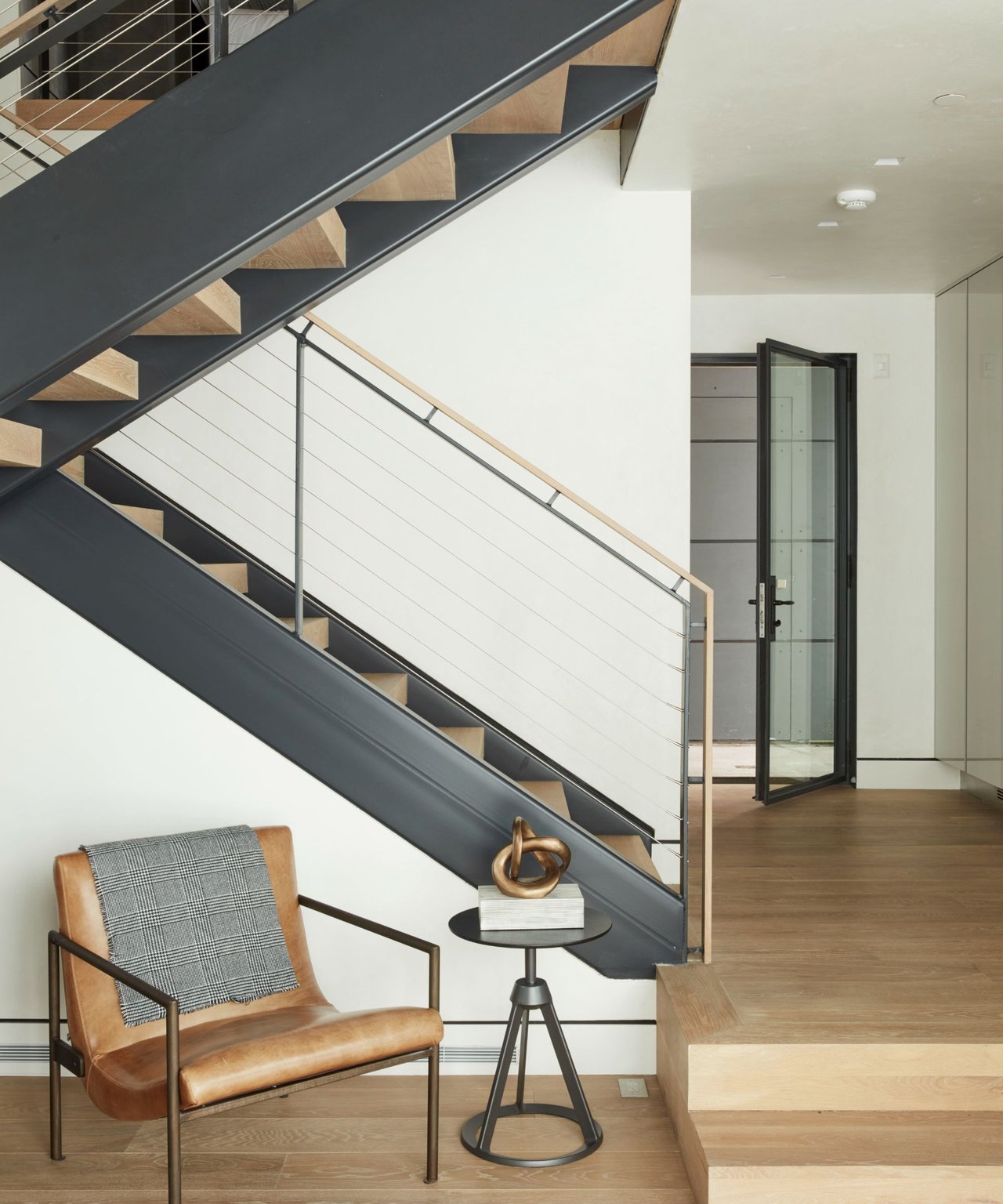 Modern interior with a dark steel staircase, pale wood treads, and a leather accent chair.