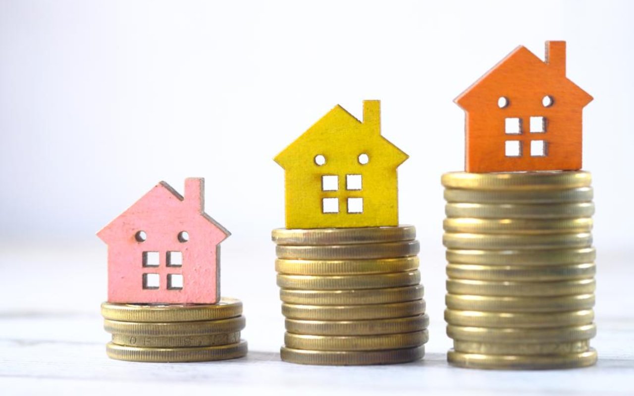 Colorful wooden houses sit on coin stacks of increasing height.