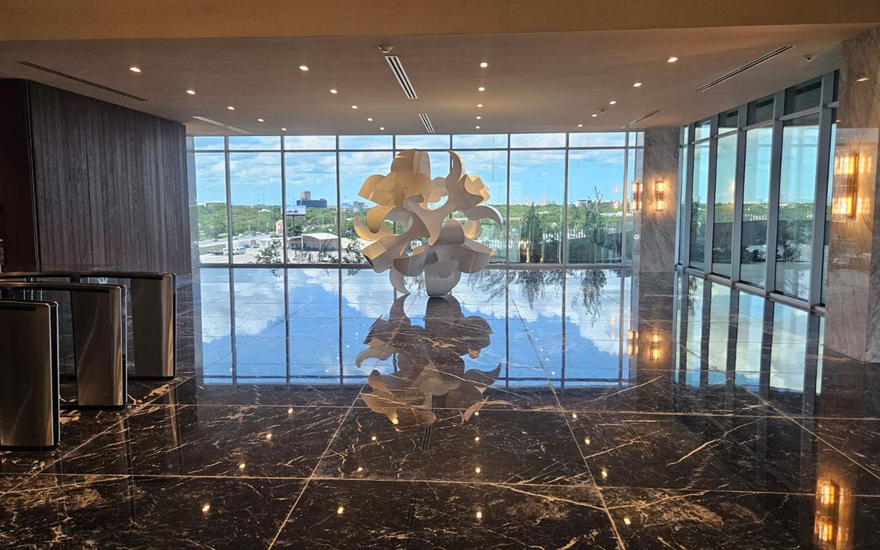 Office lobby with a reflective marble floor, floor-to-ceiling windows, and an abstract sculpture.