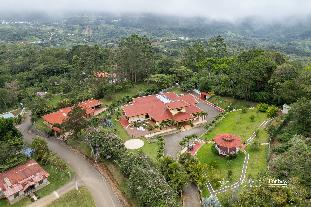 Aerial view of a red-roofed mountain home, landscaped grounds, and gazebo overlooking a green valley.