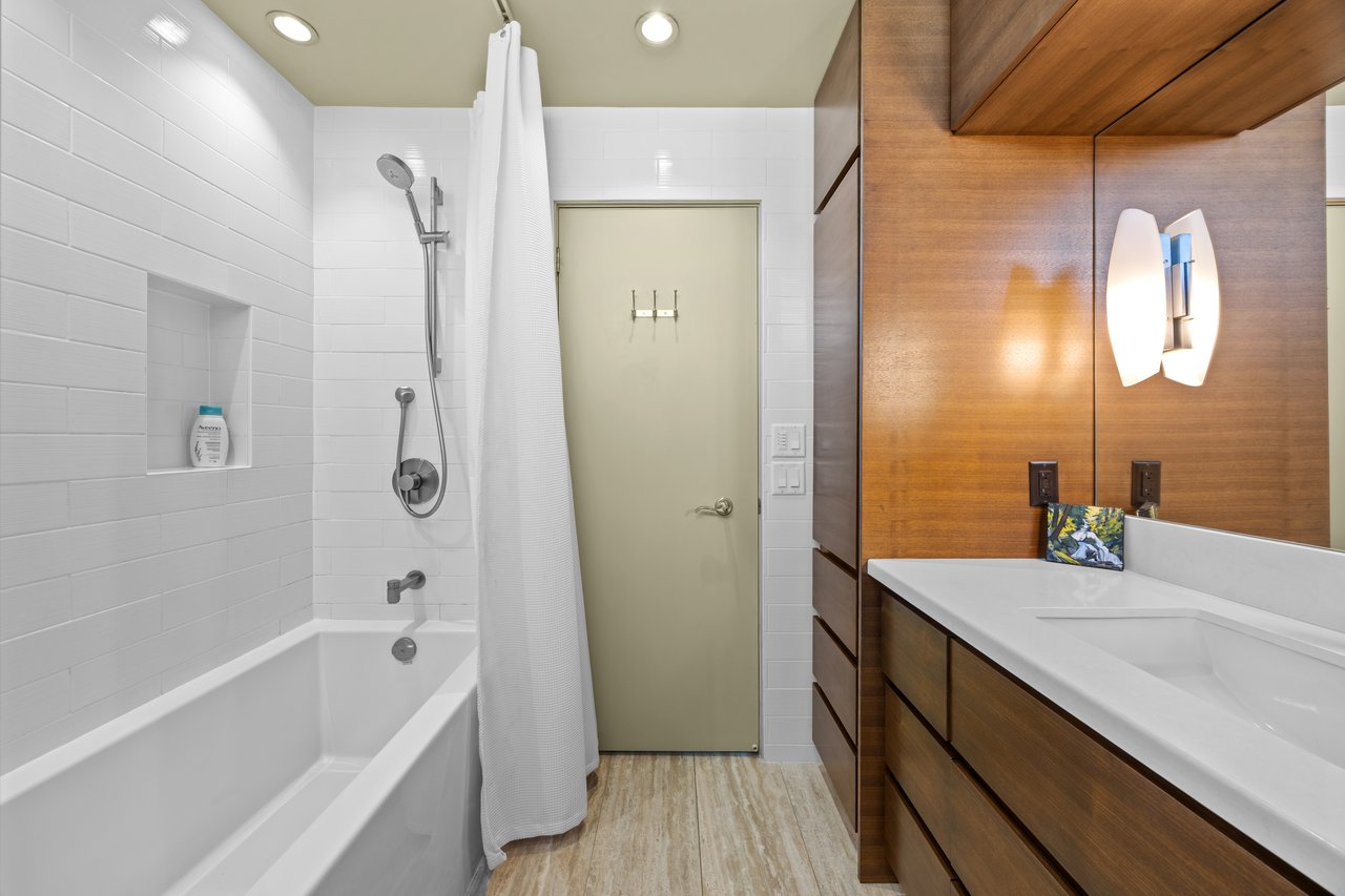 Modern bathroom with a tiled tub and shower beside a long wood vanity.